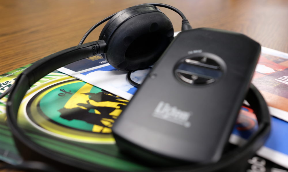 An audio description device and headset rest on a stack of playbills.