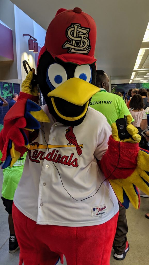 St. Louis Cardinals mascot Fredbird holds up an audio description device and holds a headset to his ear.