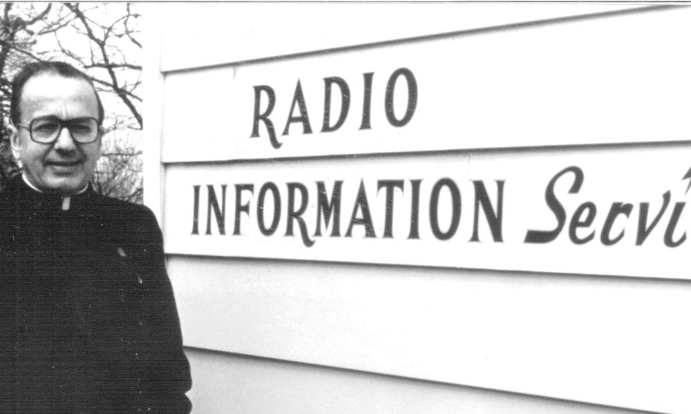 A black and white photo of Fr. Boniface Wittenbrink, OMI next to the building with the words Radio Information Service.