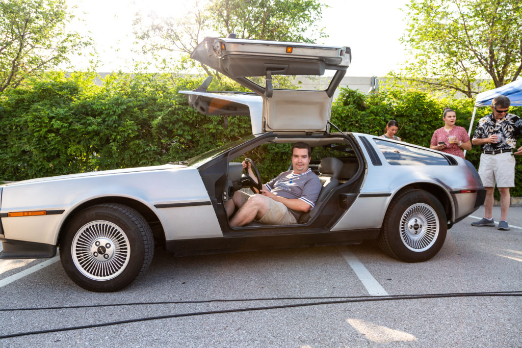 Casey Scott sits in a delorean with both gullwing doors open