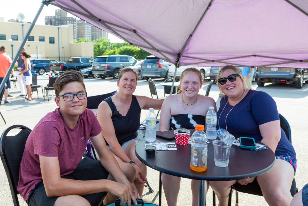 Nick, Erika, and Lexi Fuess sit around a table in a parking lot with Erin Frazier