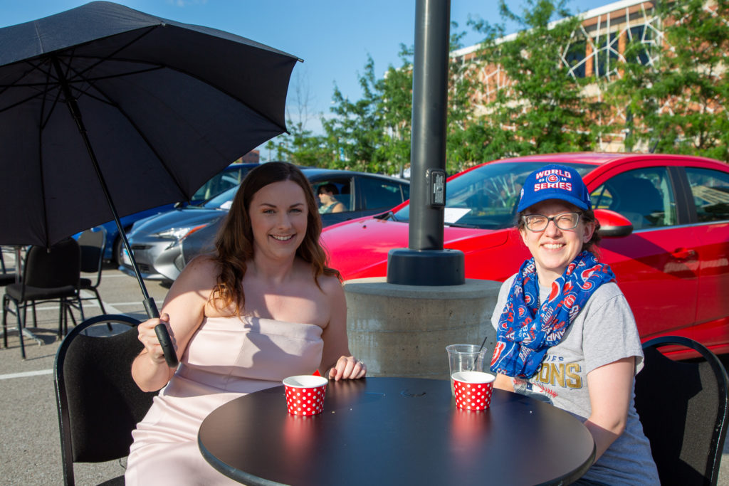 Molly Stehn and her guest sit at a table in the parking lot of the Sheldon smiling at the camera