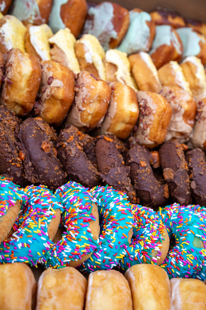 An array of donuts, some with multicolored sprinkles, bacon, or chocolate.