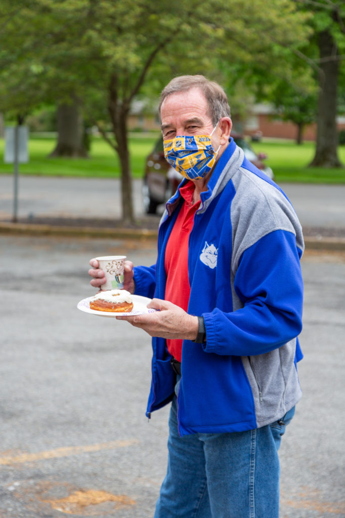 Ken Pajares wearing a SLU Billikens jacket and a Blues facemask holding a doughnut and a cup of coffee
