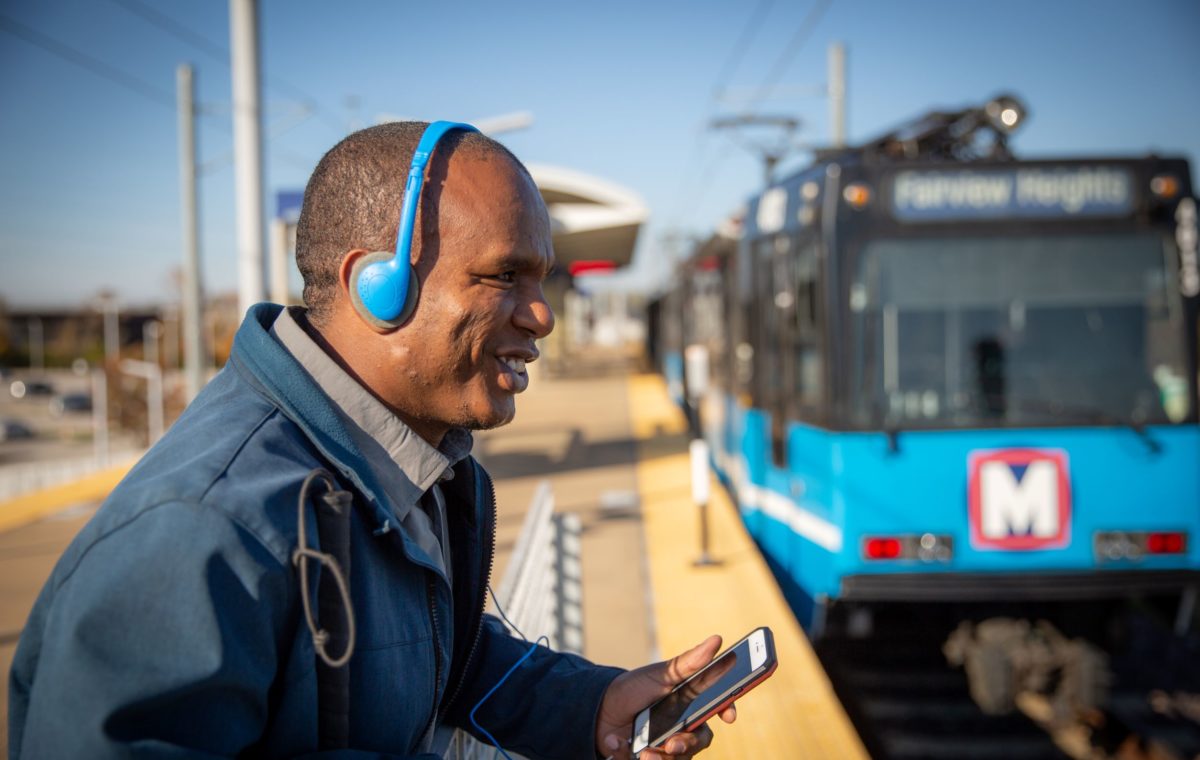 Leul smiles while listening to Headphones in front of an oncoming Metro Link Train