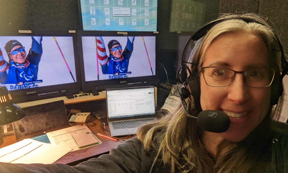 Magan smiles, wearing a headset with a skiier visible on a screens behind her.