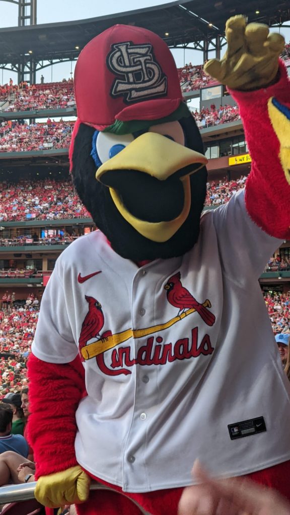Fredbird holds one hand in the air. He’s waving at Magan, who is not in the picture but is definitely freaking out to have Fredbird’s attention. 
