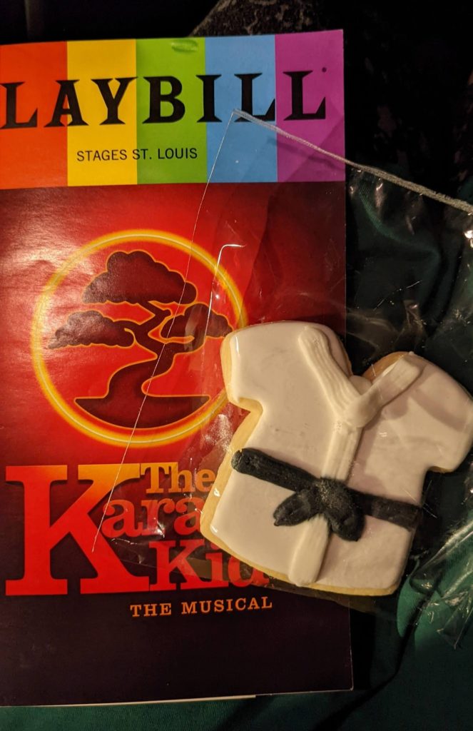 The Karate Kid Playbill and an iced cookie shaped like a white karate uniform gi with a tied black belt.