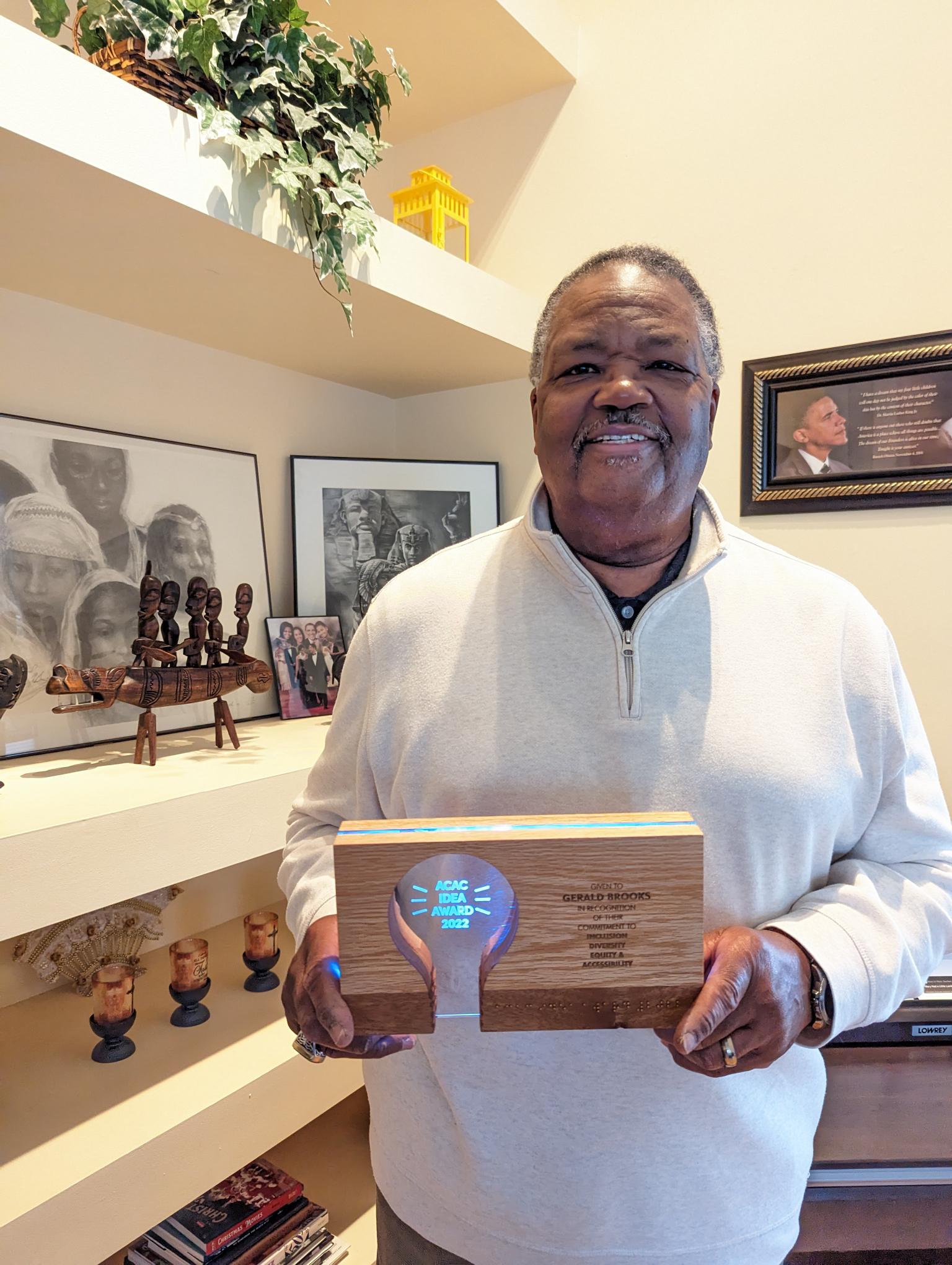 Gerald holds his award in his home. The lightbulb inside the award is lit. 