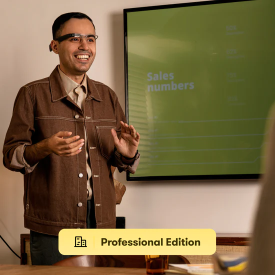 A smiling man in business casual attire wearing smart glasses, standing in front of a screen that says "Sales numbers"
