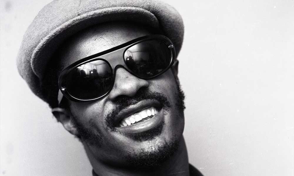 A black and white photo of a young Stevie Wonder smiling for the camera.
