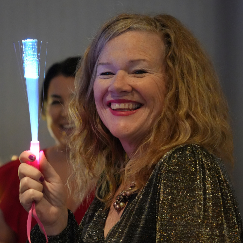 Patty wears a smile and sparkling gold top and holds up a glowing fiber optic wand.