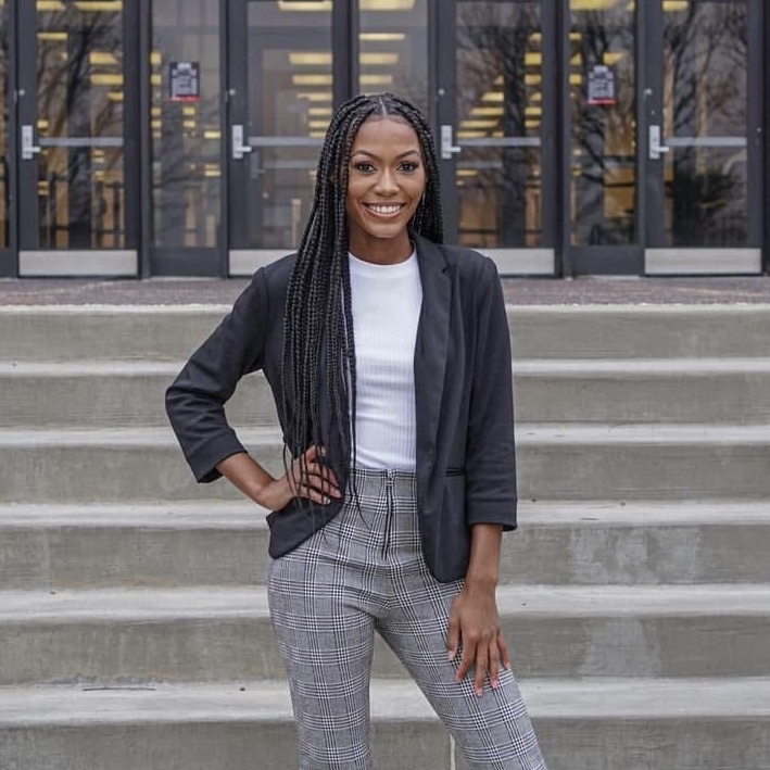Jada with her hand on her hip in business casual clothes standing on concrete steps with glass windows behind